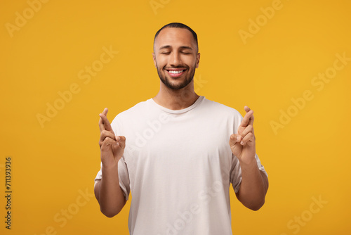 Happy man crossing his fingers on orange background