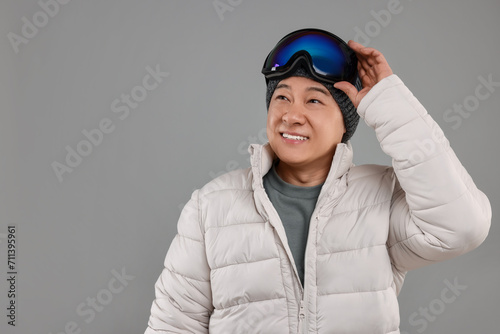 Winter sports. Happy man with ski goggles on grey background, space for text