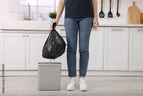 Woman taking garbage bag out of trash bin in kitchen, closeup