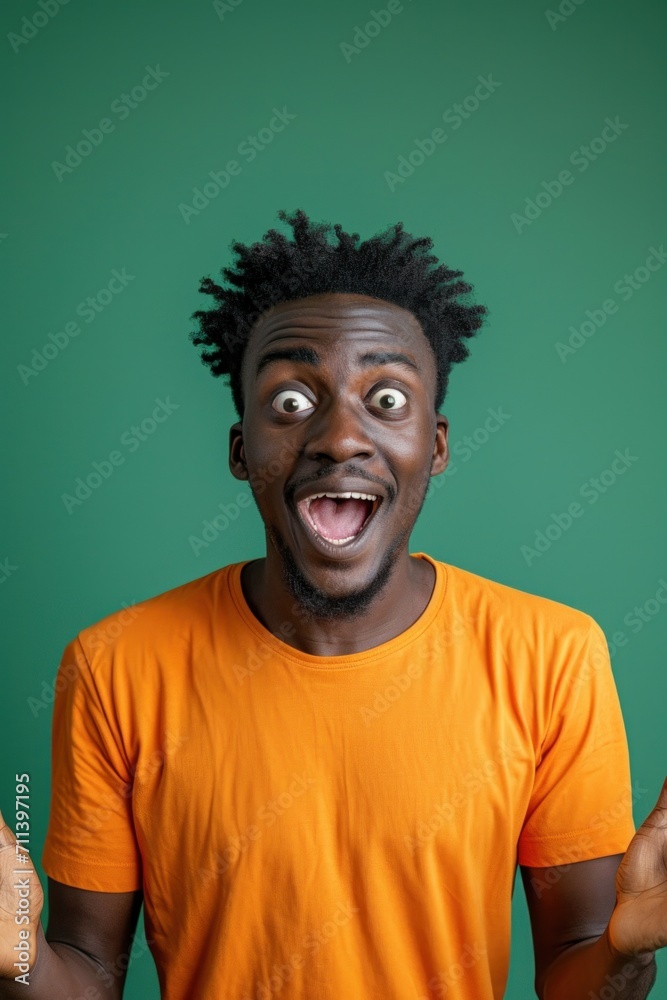 Portrait Young surprised shocked happy man of African American ethnicity. Orange t-shirt green background studio Portrait Young surprised shocked happy man of African American ethnicity. Orange t-shirt green background studio