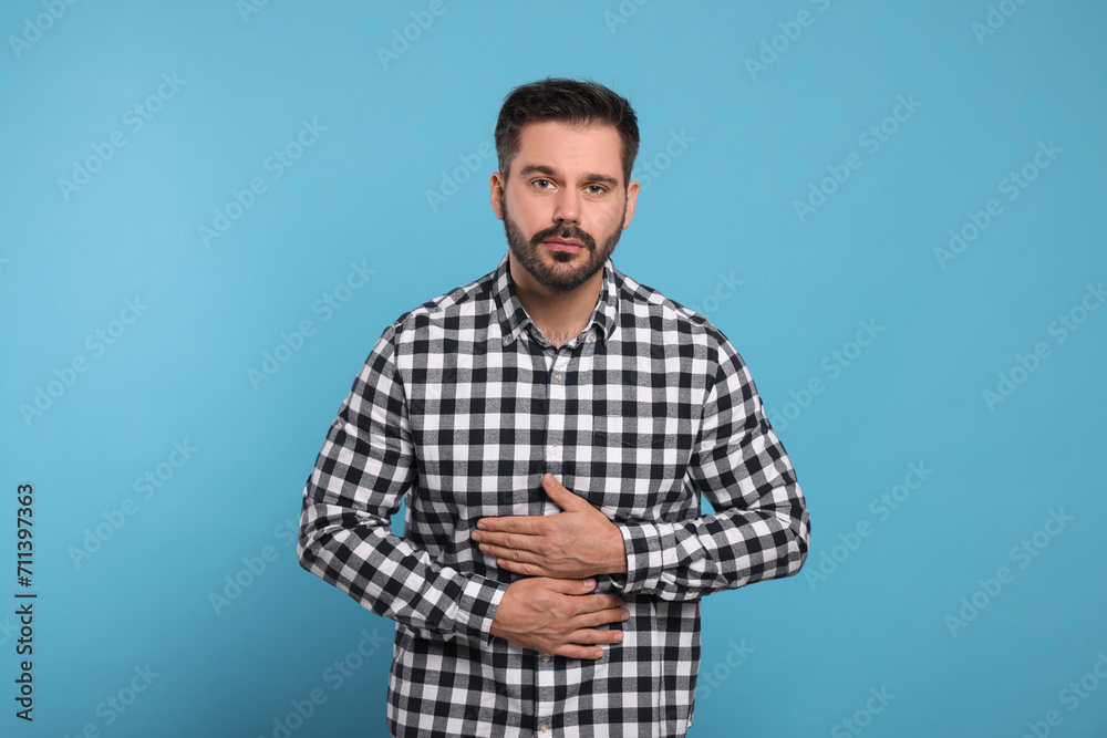 Man suffering from stomach pain on light blue background Man suffering from stomach pain on light blue background