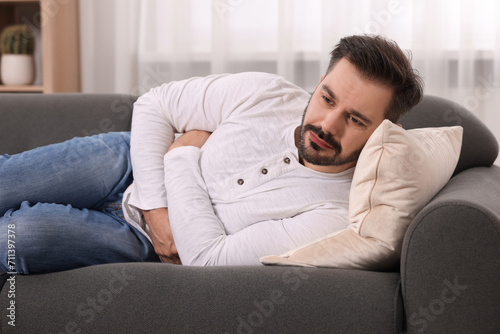 Man suffering from stomach pain on sofa at home © New Africa