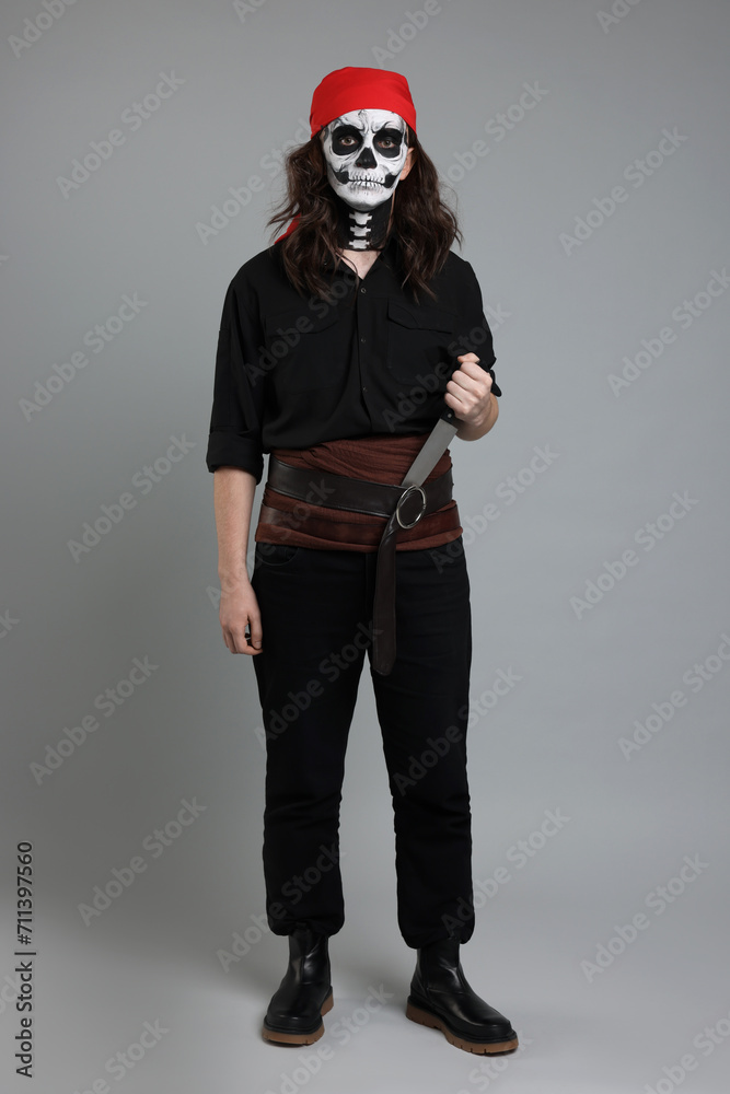 Man in scary pirate costume with skull makeup and knife on light grey background. Halloween celebration Man in scary pirate costume with skull makeup and knife on light grey background. Halloween celebration
