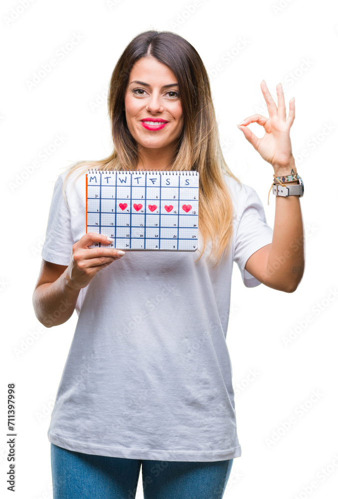 Young beautiful woman holding menstruation calendar over isolated background doing ok sign with fingers, excellent symbol Young beautiful woman holding menstruation calendar over isolated background doing ok sign with fingers, excellent symbol