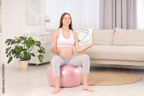 Pregnant woman meditating on fitness ball in room. Home yoga