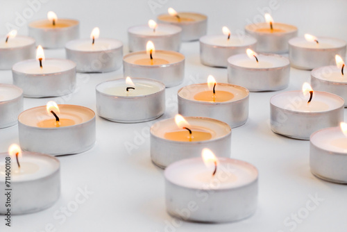 Tableau sur toile Many small round candles,tealight burns on a white background,conceptual image