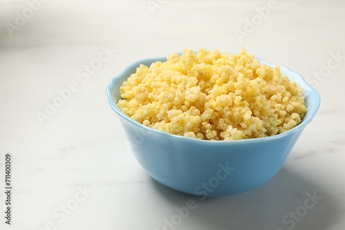 Tasty millet porridge in bowl on white marble table, closeup. Space for text