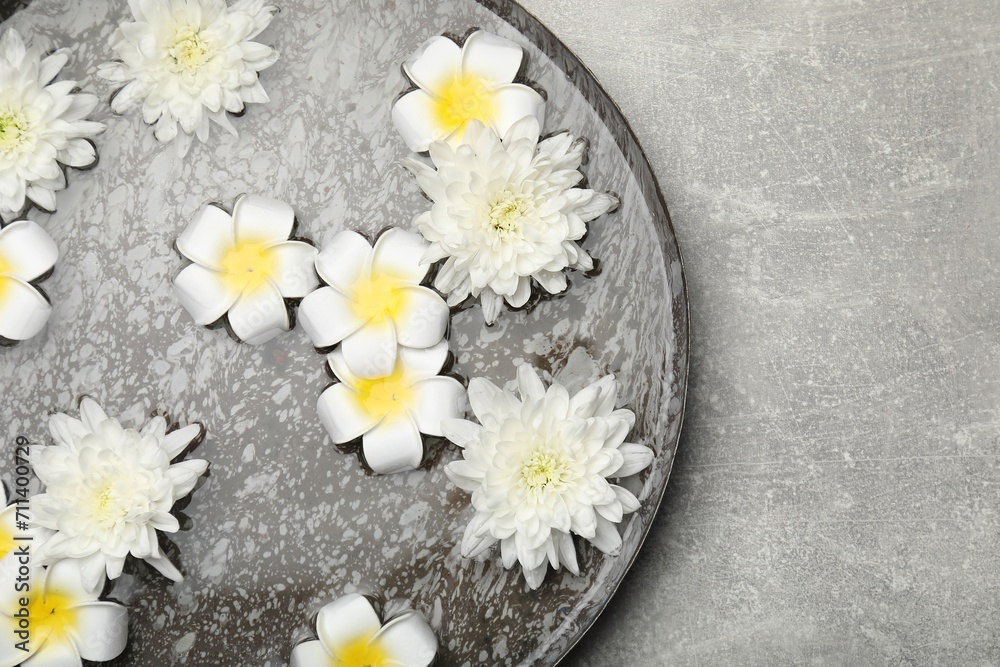 Bowl of water with flowers on light grey table, top view and space for text. Spa treatment