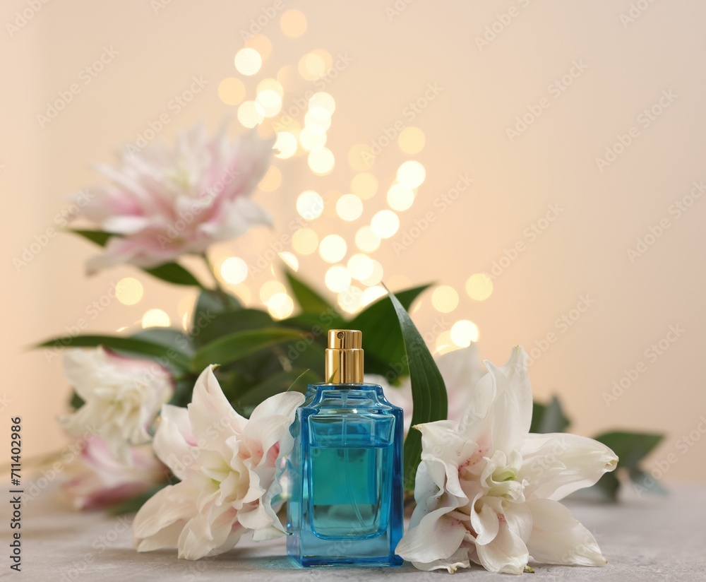 Bottle of perfume and beautiful lily flowers on table against beige background with blurred lights, closeup Bottle of perfume and beautiful lily flowers on table against beige background with blurred lights, closeup