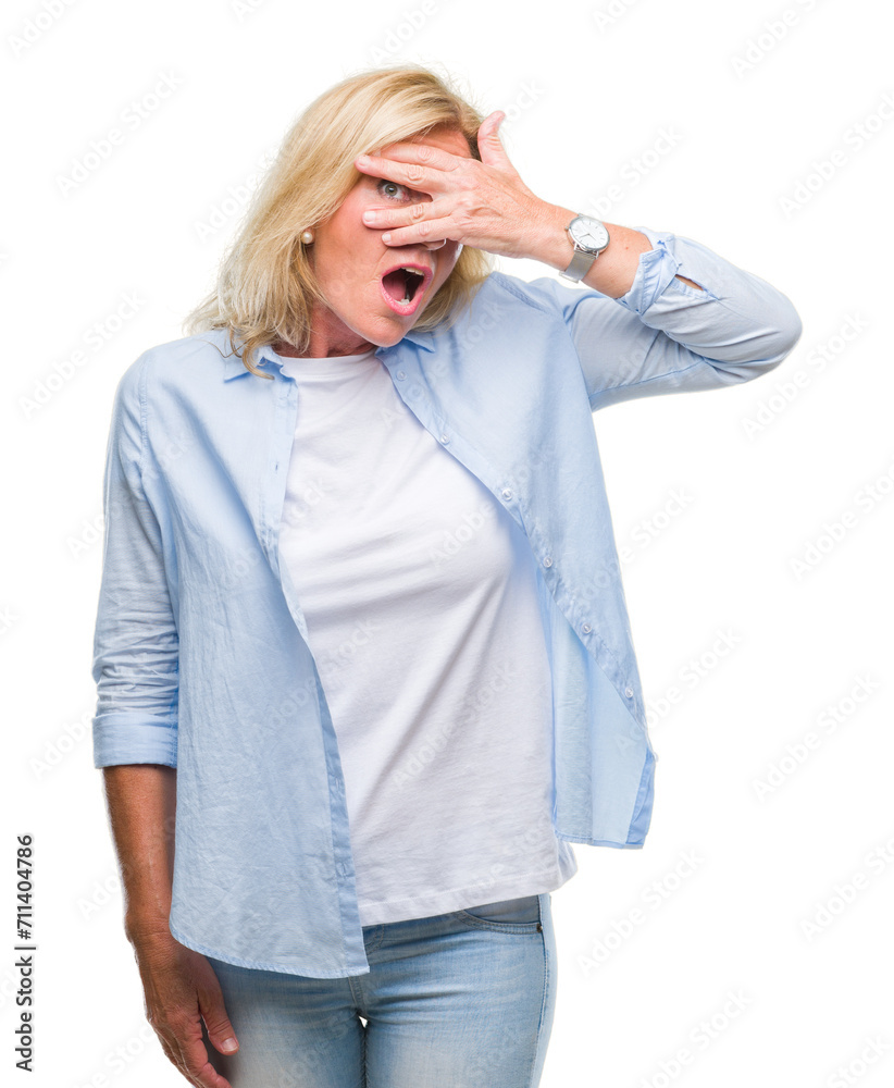 Middle age blonde woman over isolated background peeking in shock covering face and eyes with hand, looking through fingers with embarrassed expression. Middle age blonde woman over isolated background peeking in shock covering face and eyes with hand, looking through fingers with embarrassed expression.