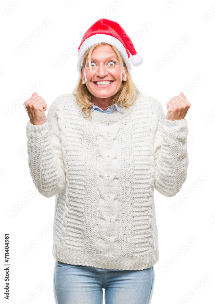 Middle age blonde woman wearing christmas hat over isolated background celebrating surprised and amazed for success with arms raised and open eyes. Winner concept. Middle age blonde woman wearing christmas hat over isolated background celebrating surprised and amazed for success with arms raised and open eyes. Winner concept.