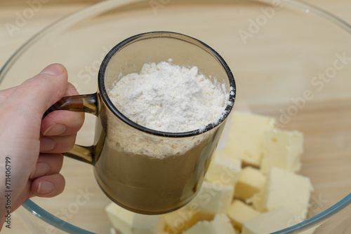 Trzymać szklankę z białą mąką nad miską z masłem, robić ciasto