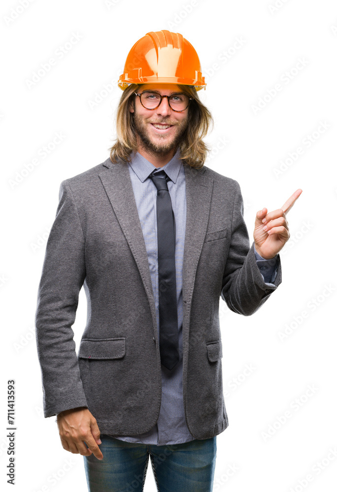 Young handsome architec man with long hair wearing safety helmet over isolated background with a big smile on face, pointing with hand and finger to the side looking at the camera. Young handsome architec man with long hair wearing safety helmet over isolated background with a big smile on face, pointing with hand and finger to the side looking at the camera.