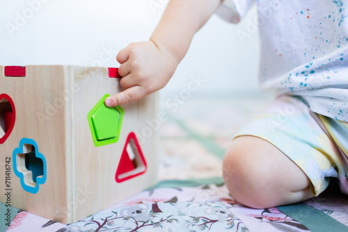 Toddler posting coloured shapes into wooden shape sorter box