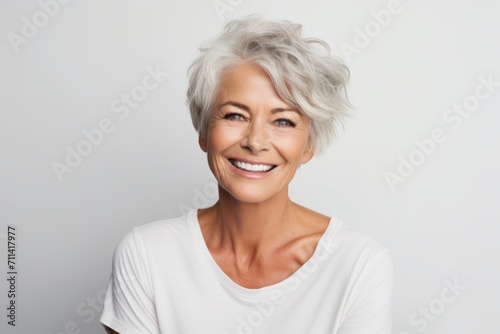 Cheerful mature woman looking at camera and smiling while standing against grey background