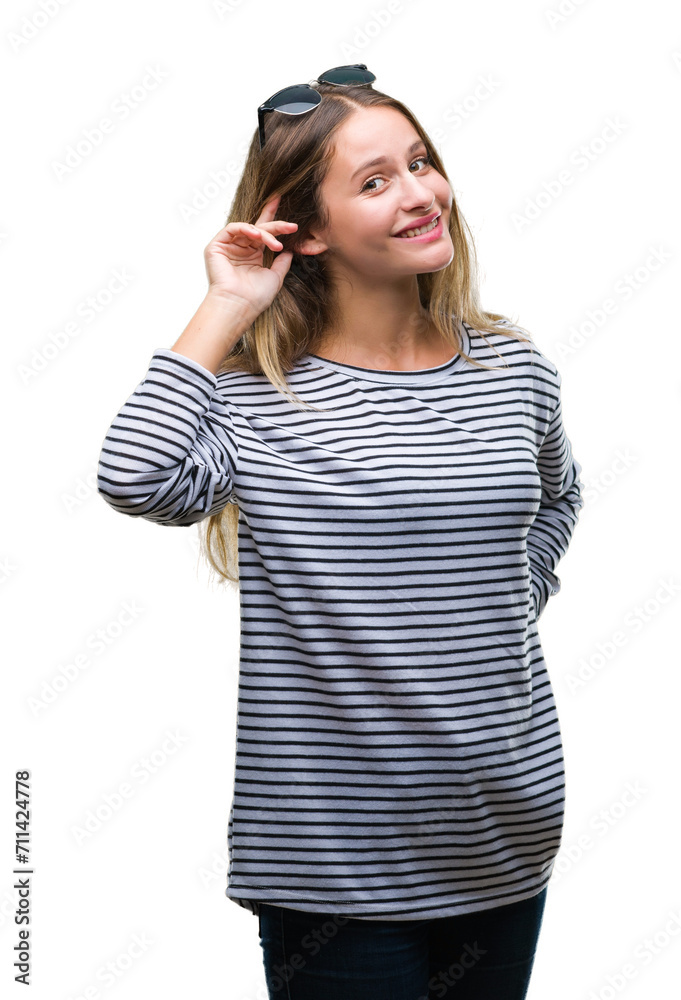Young beautiful blonde woman wearing sunglasses over isolated background smiling with hand over ear listening an hearing to rumor or gossip. Deafness concept. Young beautiful blonde woman wearing sunglasses over isolated background smiling with hand over ear listening an hearing to rumor or gossip. Deafness concept.