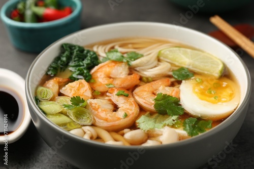 Delicious ramen with shrimps and egg in bowl on grey table, closeup. Noodle soup