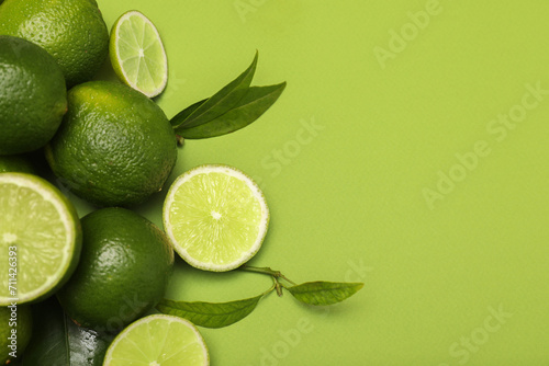 Pile of fresh limes and leaves on green background, flat lay. Space for text