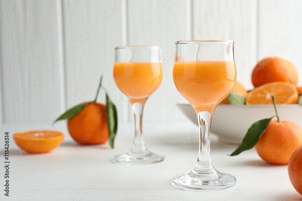 Tasty tangerine liqueur in glasses and fresh fruits on white table. Space for text