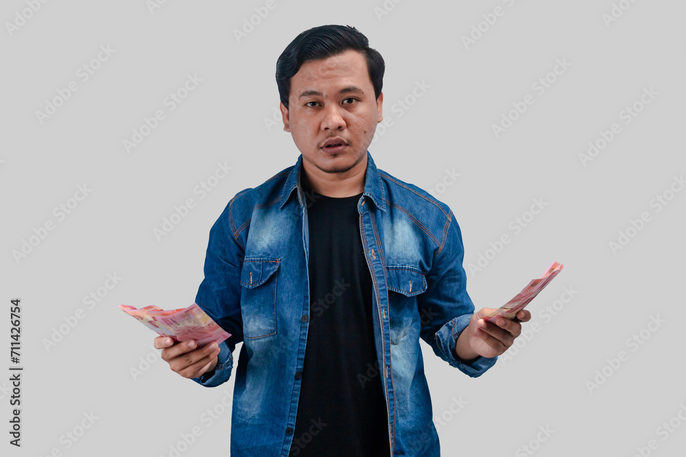 Young Asian man showing confused face expression while holding paper money