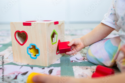 Toddler posting coloured shapes into wooden shape sorter box photo