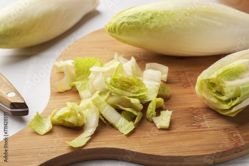 Fresh raw Belgian endives (chicory) and wooden board on white tiled table, closeup