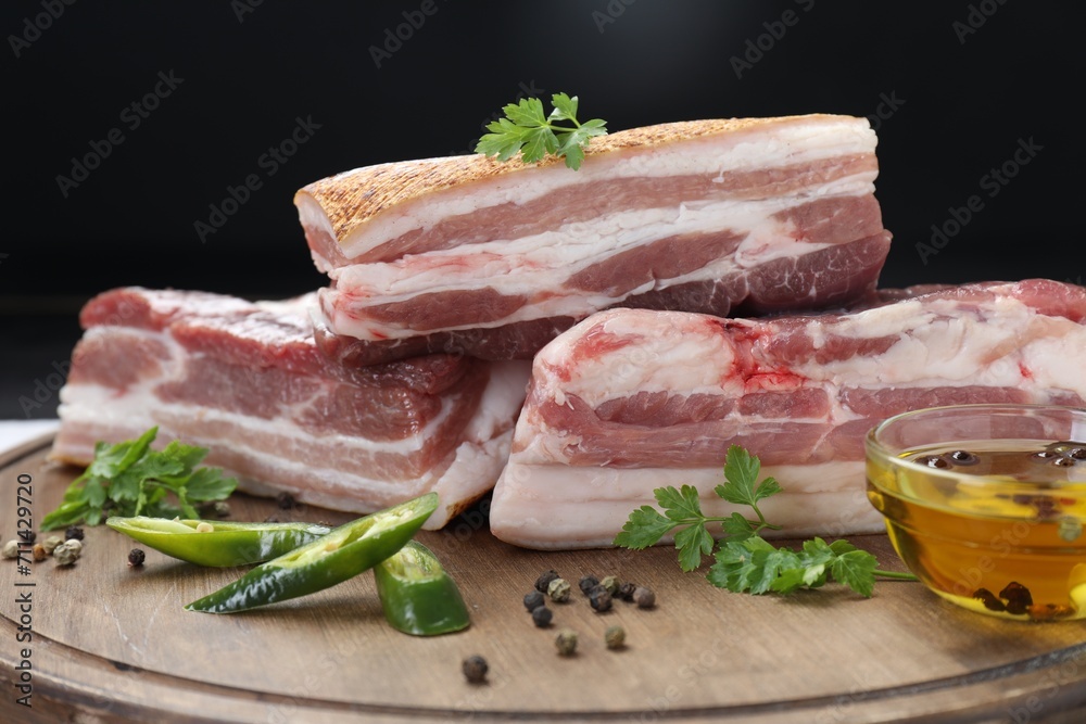 Pieces of raw pork belly, chili pepper, peppercorns, oil and parsley on wooden board, closeup