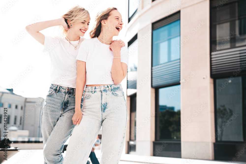 Two young beautiful smiling hipster female in trendy summer white t-shirt and jeans clothes. Carefree women posing in the street. Positive models having fun outdoors. Cheerful and happy Two young beautiful smiling hipster female in trendy summer white t-shirt and jeans clothes. Carefree women posing in the street. Positive models having fun outdoors. Cheerful and happy