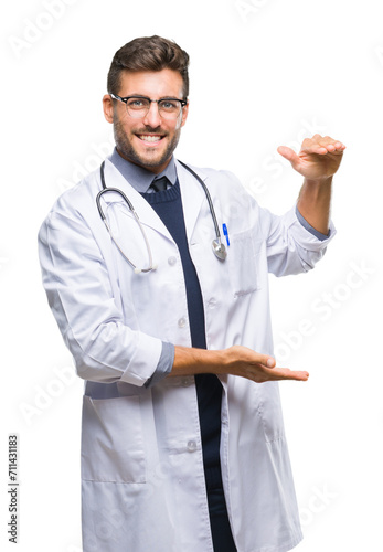 Young handsome doctor man over isolated background gesturing with hands showing big and large size sign, measure symbol. Smiling looking at the camera. Measuring concept.