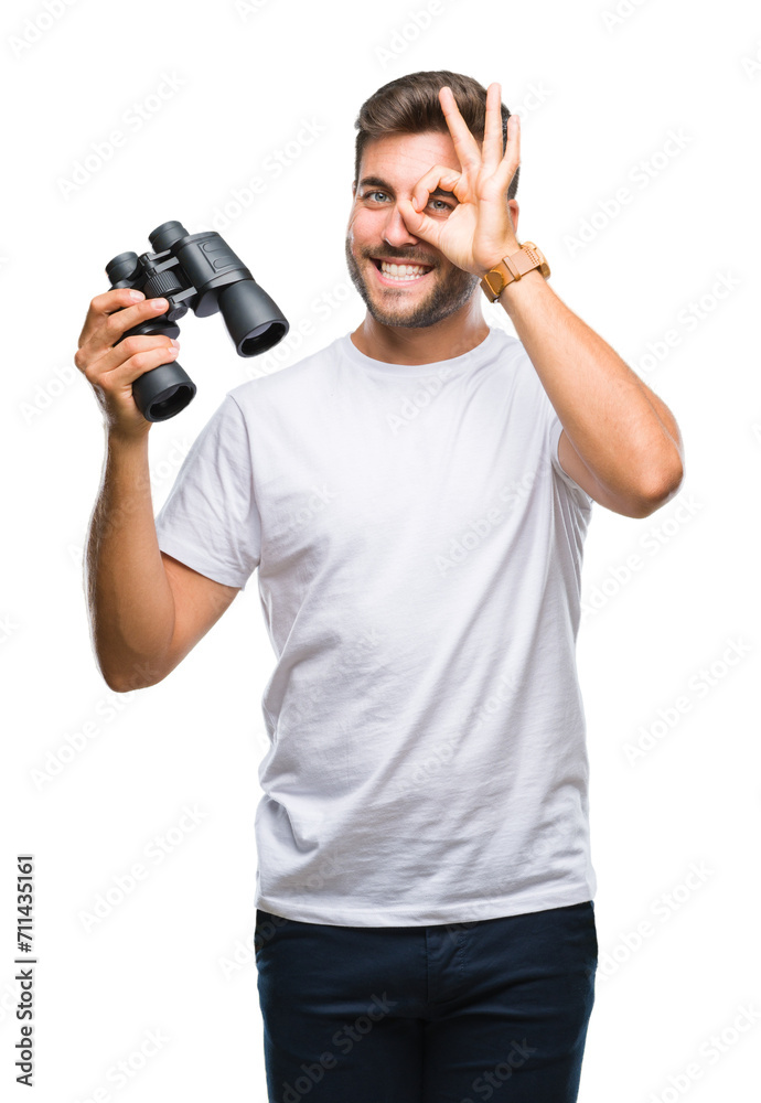Young handsome man looking through binoculars over isolated background with happy face smiling doing ok sign with hand on eye looking through fingers Young handsome man looking through binoculars over isolated background with happy face smiling doing ok sign with hand on eye looking through fingers