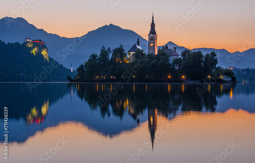 The sun sets on Lake Bled, casting a warm glow on the Pilgrimage Church of the Assumption of Maria and the Bled Castle photo