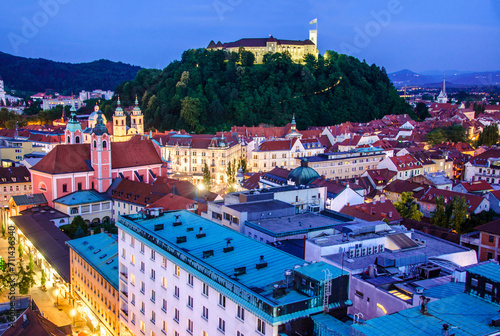 Night falls on Ljubljana with a view of the castle overlooking the city's glowing historical architecture and streets photo