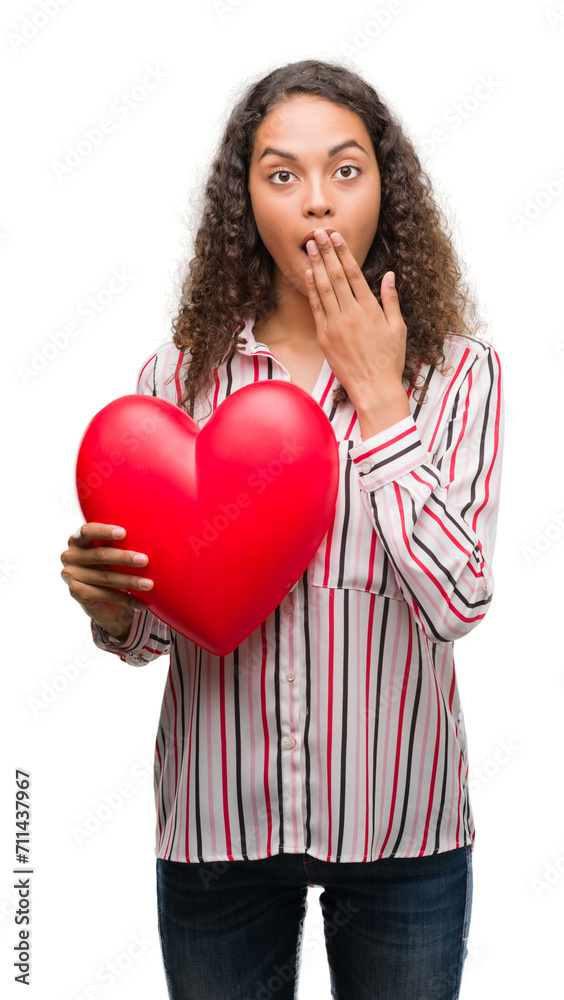 Young hispanic woman in love holding red heart cover mouth with hand shocked with shame for mistake, expression of fear, scared in silence, secret concept Young hispanic woman in love holding red heart cover mouth with hand shocked with shame for mistake, expression of fear, scared in silence, secret concept