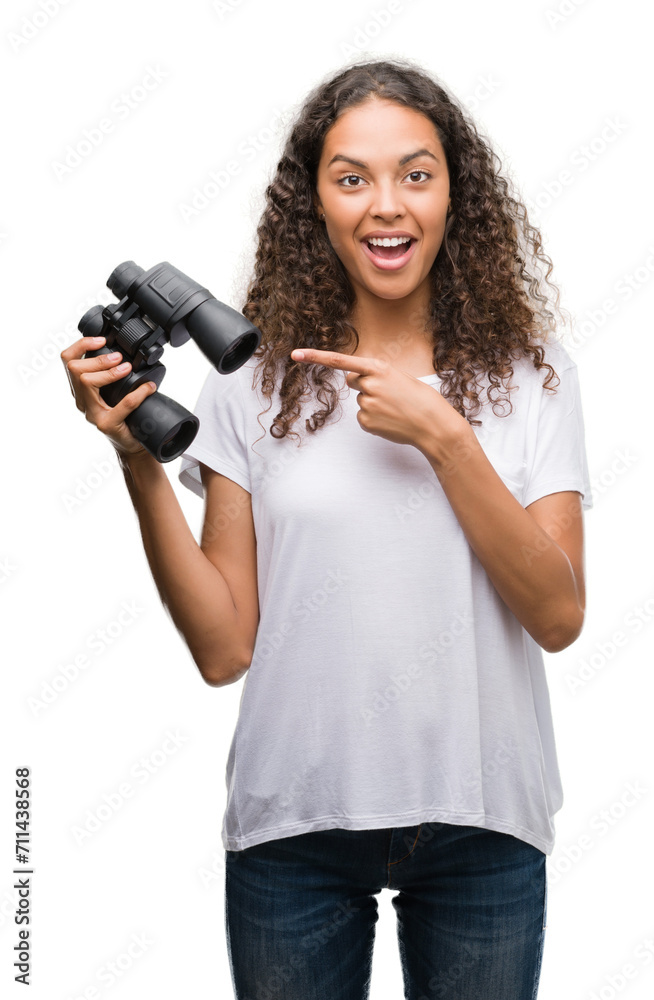 Young hispanic woman looking through binoculars very happy pointing with hand and finger Young hispanic woman looking through binoculars very happy pointing with hand and finger