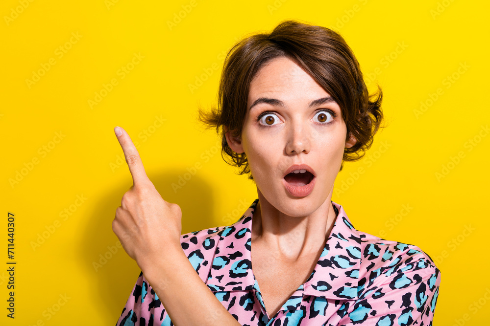 Photo of pretty impressed lady open mouth indicate finger empty space isolated on yellow color background Photo of pretty impressed lady open mouth indicate finger empty space isolated on yellow color background