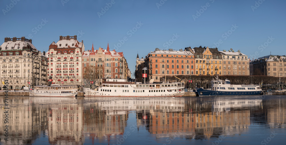 Hotel, steam commuter ferries and boats at the pier Strandvägen at the icy bay Nybroviken a part of the Ladugårdslandsviken a sunny winter day in Stockholm