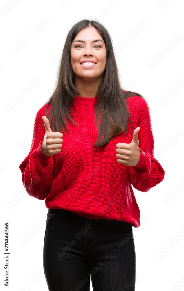 Young beautiful hispanic wearing red sweater success sign doing positive gesture with hand, thumbs up smiling and happy. Looking at the camera with cheerful expression, winner gesture. Young beautiful hispanic wearing red sweater success sign doing positive gesture with hand, thumbs up smiling and happy. Looking at the camera with cheerful expression, winner gesture.