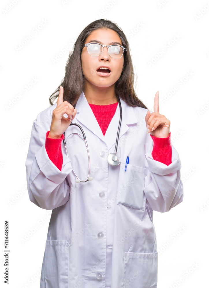 Young arab doctor woman over isolated background amazed and surprised looking up and pointing with fingers and raised arms.