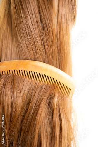 A wooden comb on a brown long shiny synthetic extensions of synthetic brown hair wig