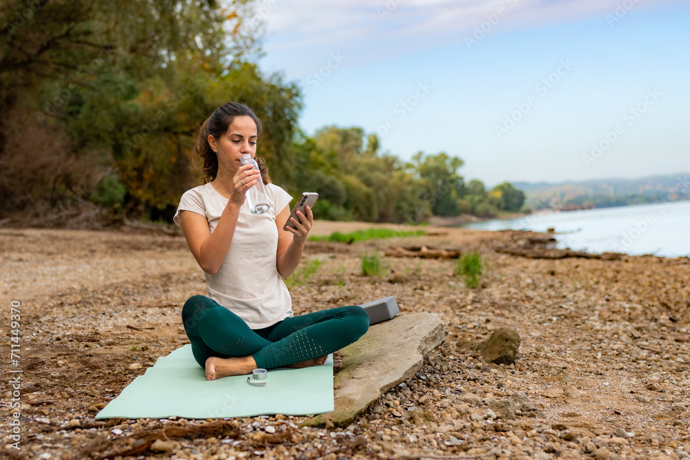 Taking a break, she hydrates with a sip from a glass bottle while sitting on her workout mat.