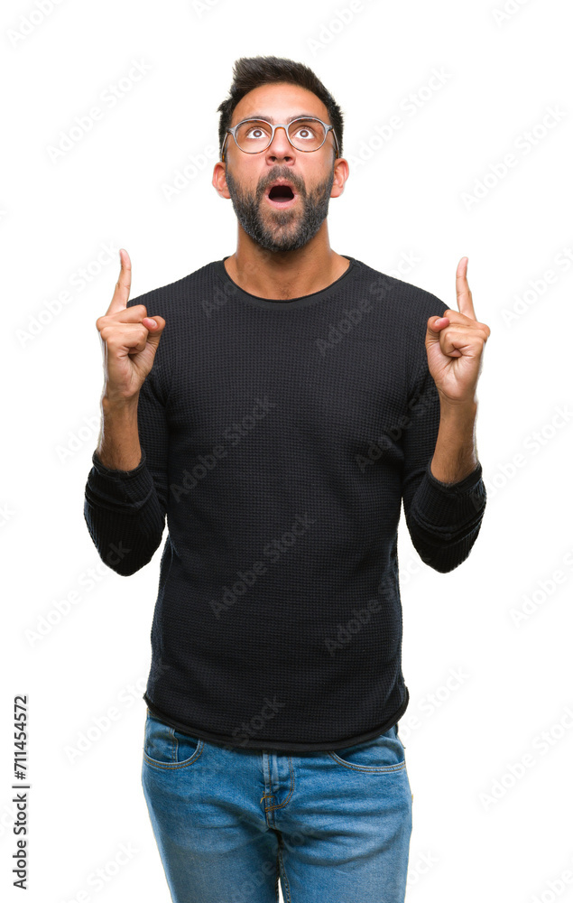 Adult hispanic man wearing glasses over isolated background amazed and surprised looking up and pointing with fingers and raised arms. Adult hispanic man wearing glasses over isolated background amazed and surprised looking up and pointing with fingers and raised arms.