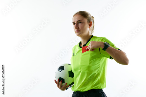 Young woman, female soccer referee holding ball, stopping game and showing red card against white studio background. Concept of sport, competition, match, profession, football game, control photo