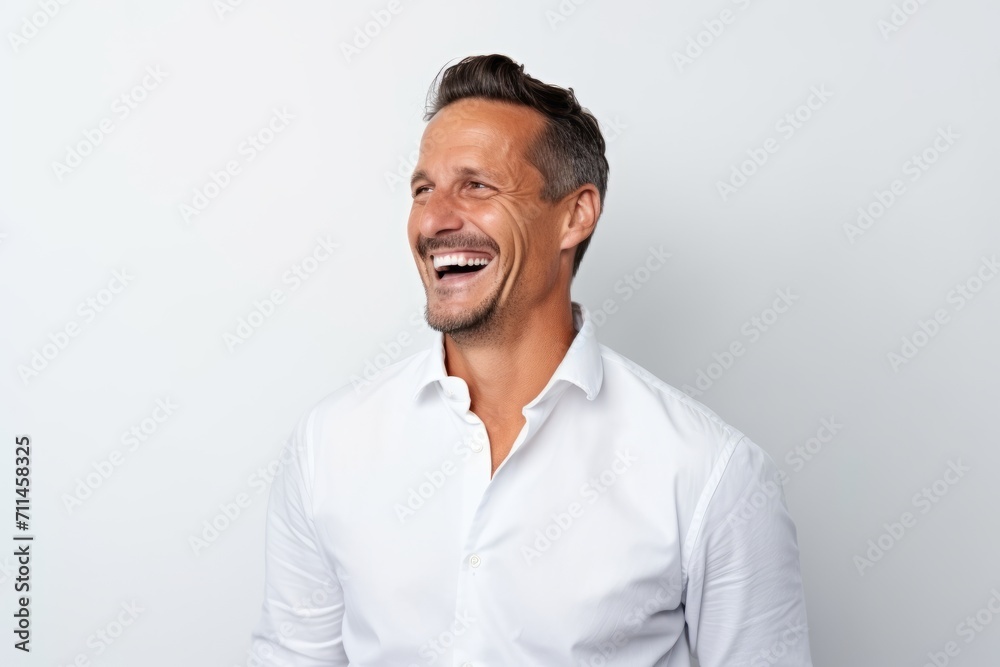 Portrait of a happy mature man laughing and looking at camera while standing against grey background