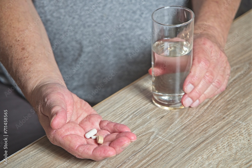 Senior man at table with medication in hand and glass of water Senior man at table with medication in hand and glass of water