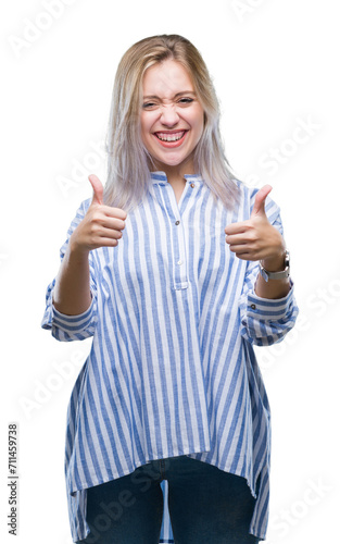 Young blonde woman over isolated background approving doing positive gesture with hand, thumbs up smiling and happy for success. Looking at the camera, winner gesture.