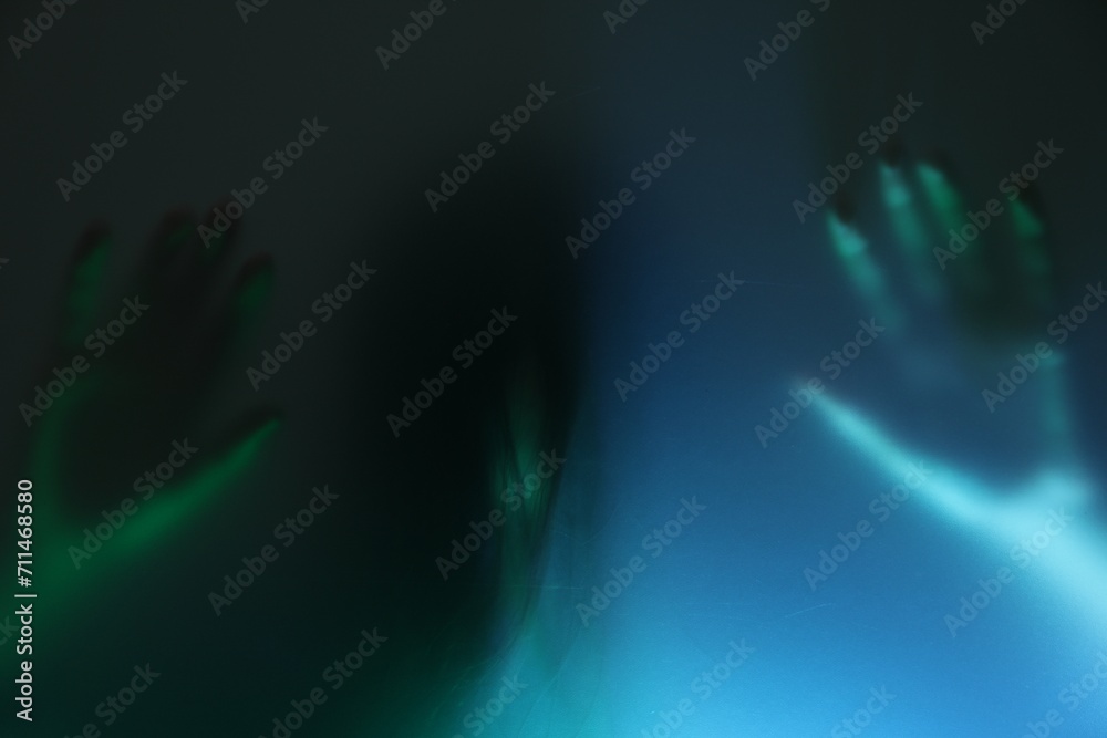 Silhouette of creepy ghost behind glass against color background Silhouette of creepy ghost behind glass against color background