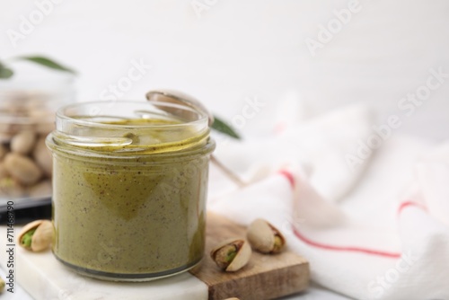 Tasty pistachio cream in jar and nuts on table  closeup. Space for text