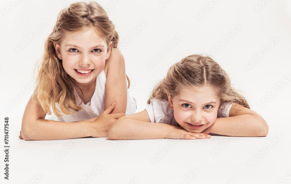 Studioportrait von zwei Schwestern am Boden liegend, barfuss in Jeans. Lächeln in die Kamera Studioportrait von zwei Schwestern am Boden liegend, barfuss in Jeans. Lächeln in die Kamera