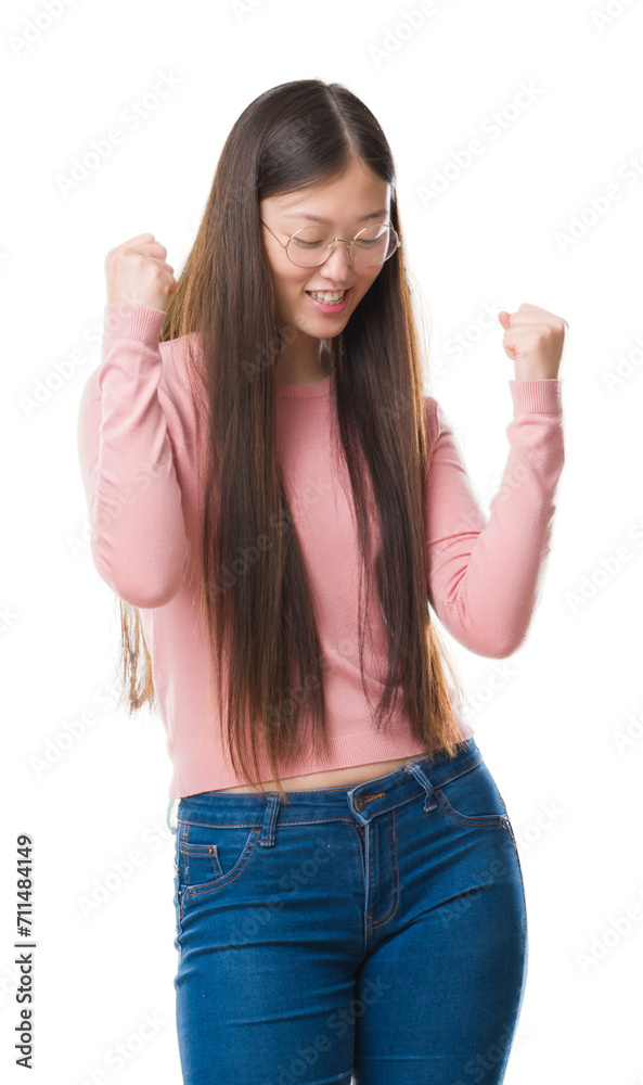 Young Chinese woman over isolated background wearing glasses very happy and excited doing winner gesture with arms raised, smiling and screaming for success. Celebration concept.