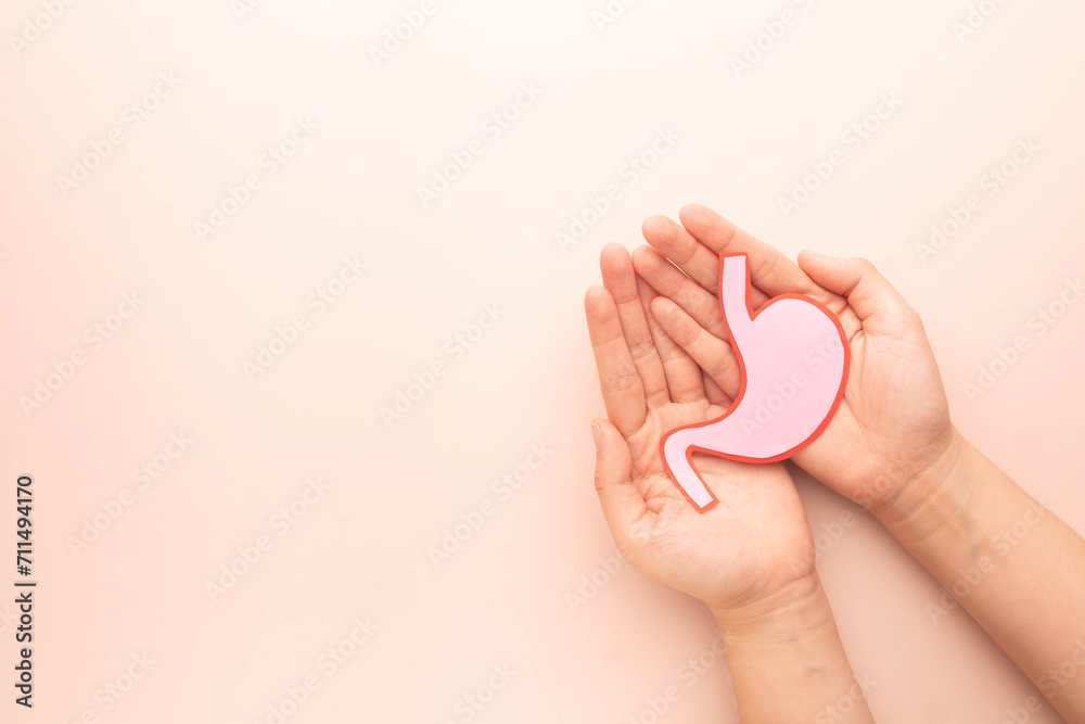 Human hands holding stomach organ made from paper on beige background. Concept of gastric cancer screening, stomach transplant, digestive tract problem and stomach disease treatment. Flat layout. - obrazy, fototapety, plakaty 